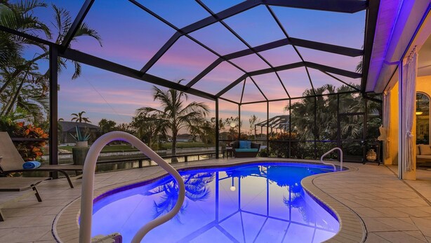 Un espace piscine doté d’une structure en verre, de palmiers et offrant une vue sur le coucher de soleil.