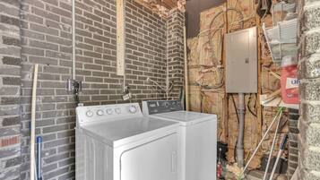 Een wasruimte met een witte wasmachine en droger, een houten balk en isolatie op de muren.
