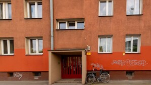 A multi-story building with a red door and windows, a bicycle parked outside, and graffiti on the wall. - Rynek Wrocław Cosy Studio (Wrocław)