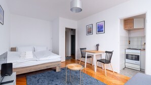 A modern bedroom with a wooden bed, a small dining area with two chairs, a kitchen with a stove, and a hallway leading to another room. - Rynek Wrocław Cosy Studio (Wrocław)