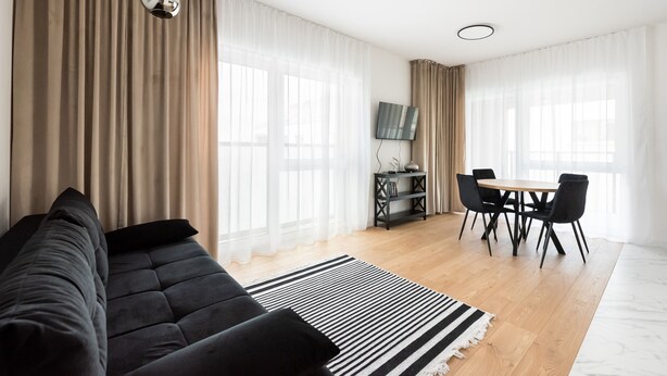 A modern living room with a black sofa, a dining table with chairs, and a flat-screen TV mounted on the wall. - Brzeziny Deluxe Apartment (Warszawa)
