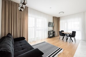 A modern living room with a black sofa, a dining table with chairs, and a flat-screen TV mounted on the wall. - Brzeziny Deluxe Apartment (Warszawa)
