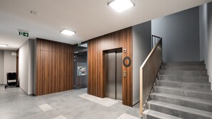 A modern interior with a wooden wall, an elevator, and a staircase. - Brzeziny Deluxe Apartment (Warszawa)