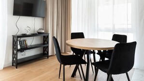 A modern dining area with a round table, black chairs, a black TV stand, and a bookshelf. - Brzeziny Deluxe Apartment (Warszawa)