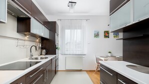 Una cucina moderna con mobili scuri, un piano di lavoro bianco e una finestra con tende leggere.