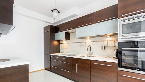 Una cucina moderna con mobili in legno scuro, un piano di lavoro bianco, elettrodomestici in acciaio inossidabile e illuminazione sotto i pensili.