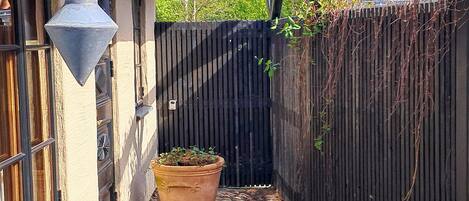 A narrow alleyway with a large terracotta pot, a wooden fence, and a building with a dark door and windows.