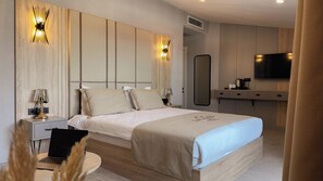 Moderni hotellihuone, jossa on suuri sänky, yöpöydät, työpöytä, tuoli, televisio ja peili.