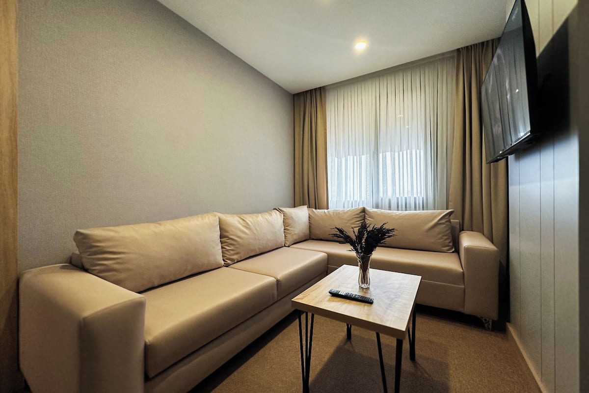 A modern living room with a beige sectional sofa, a small wooden coffee table, and a flat-screen TV mounted on the wall.