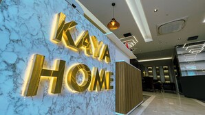 Un hall d’hôtel moderne avec un mur en marbre et une grande enseigne lumineuse sur laquelle on peut lire « KAYA HOME ».
