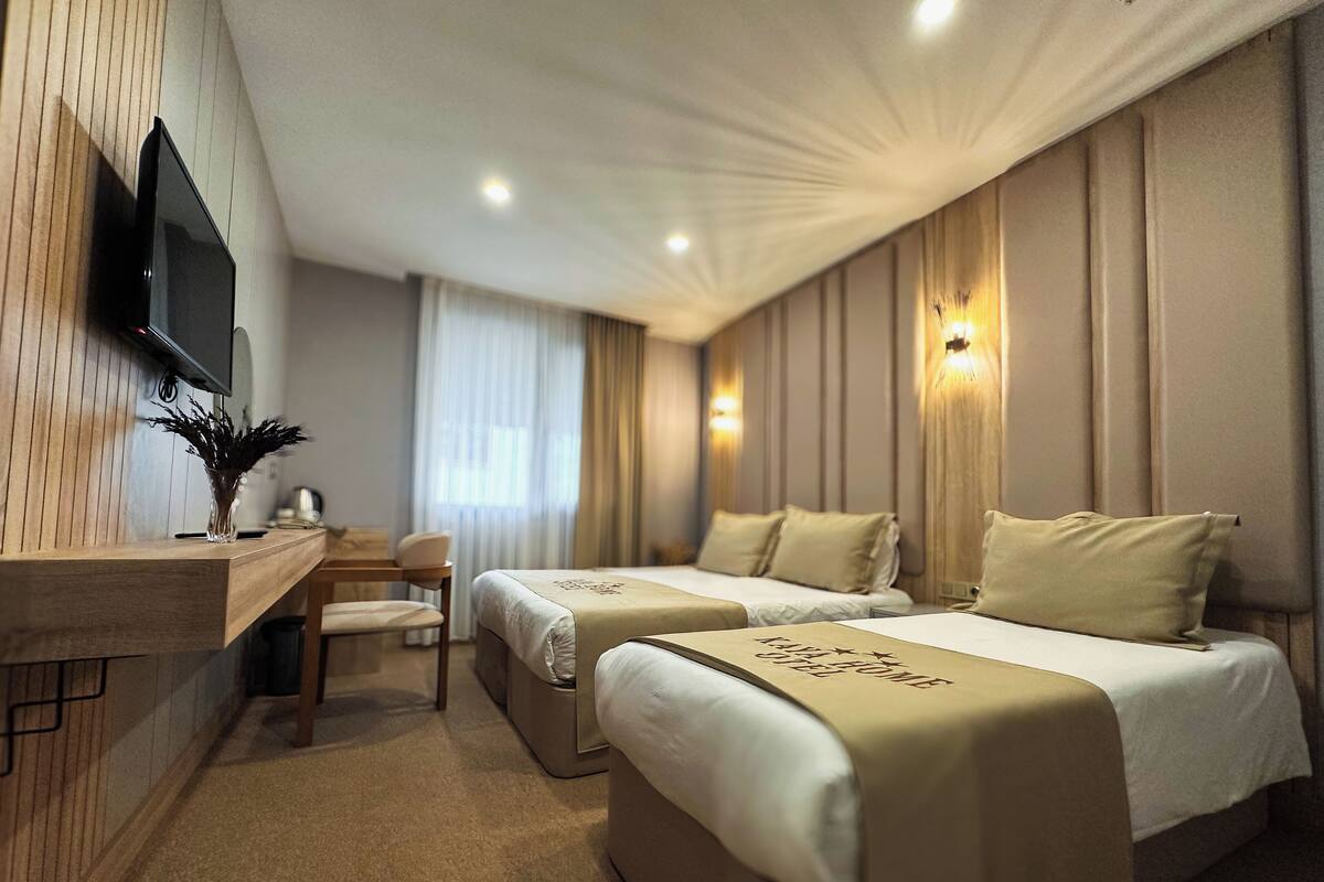 A hotel room with two beds, a desk, a chair, a TV, and a window with curtains.