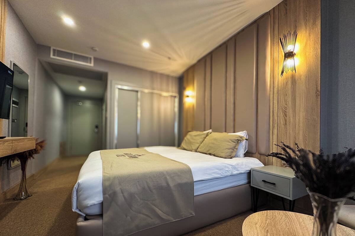 A modern hotel room with a bed, bedside table, lamp, and a view of the hallway.