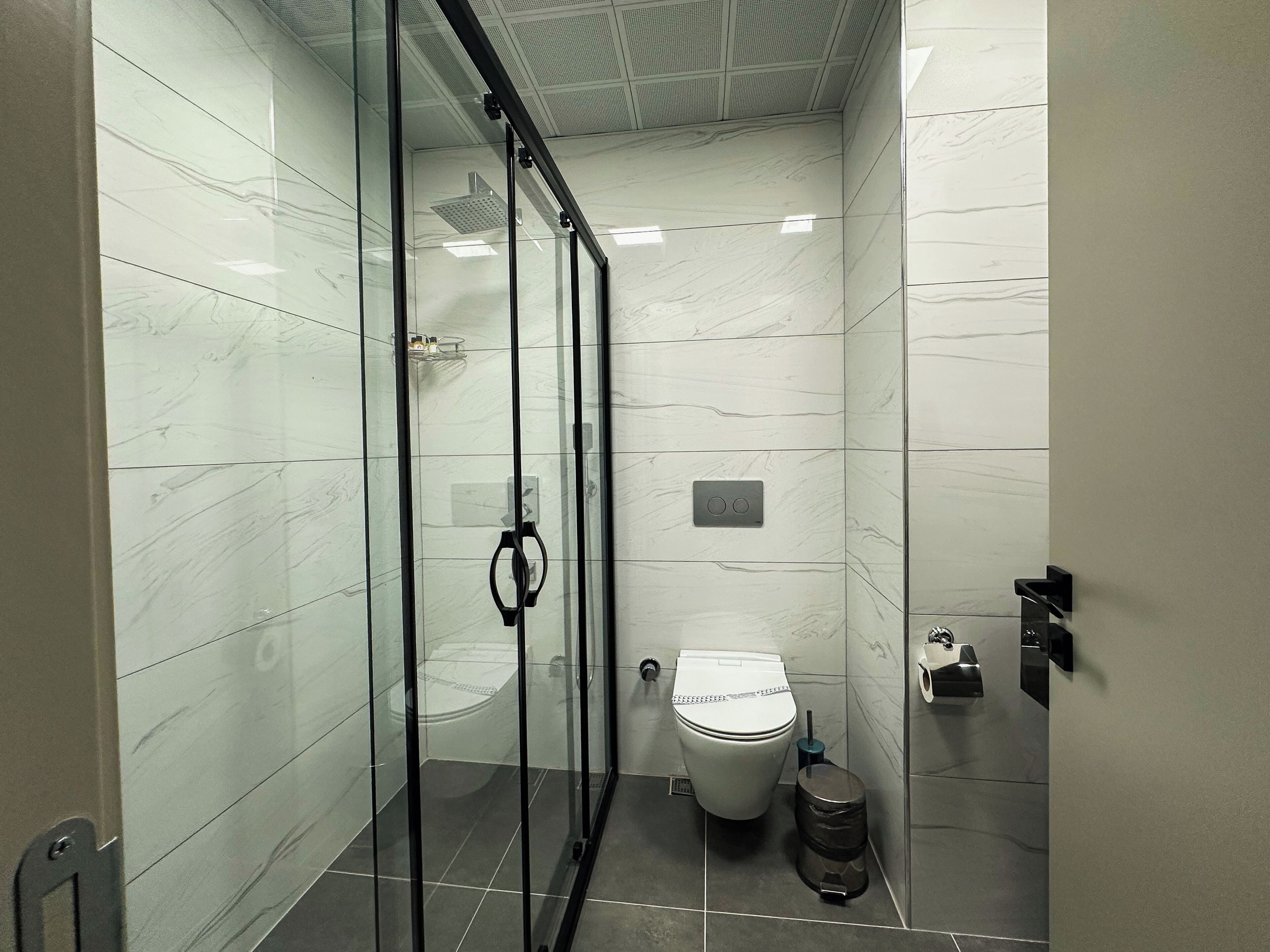 Un baño moderno con ducha de vidrio, inodoro y basurero.