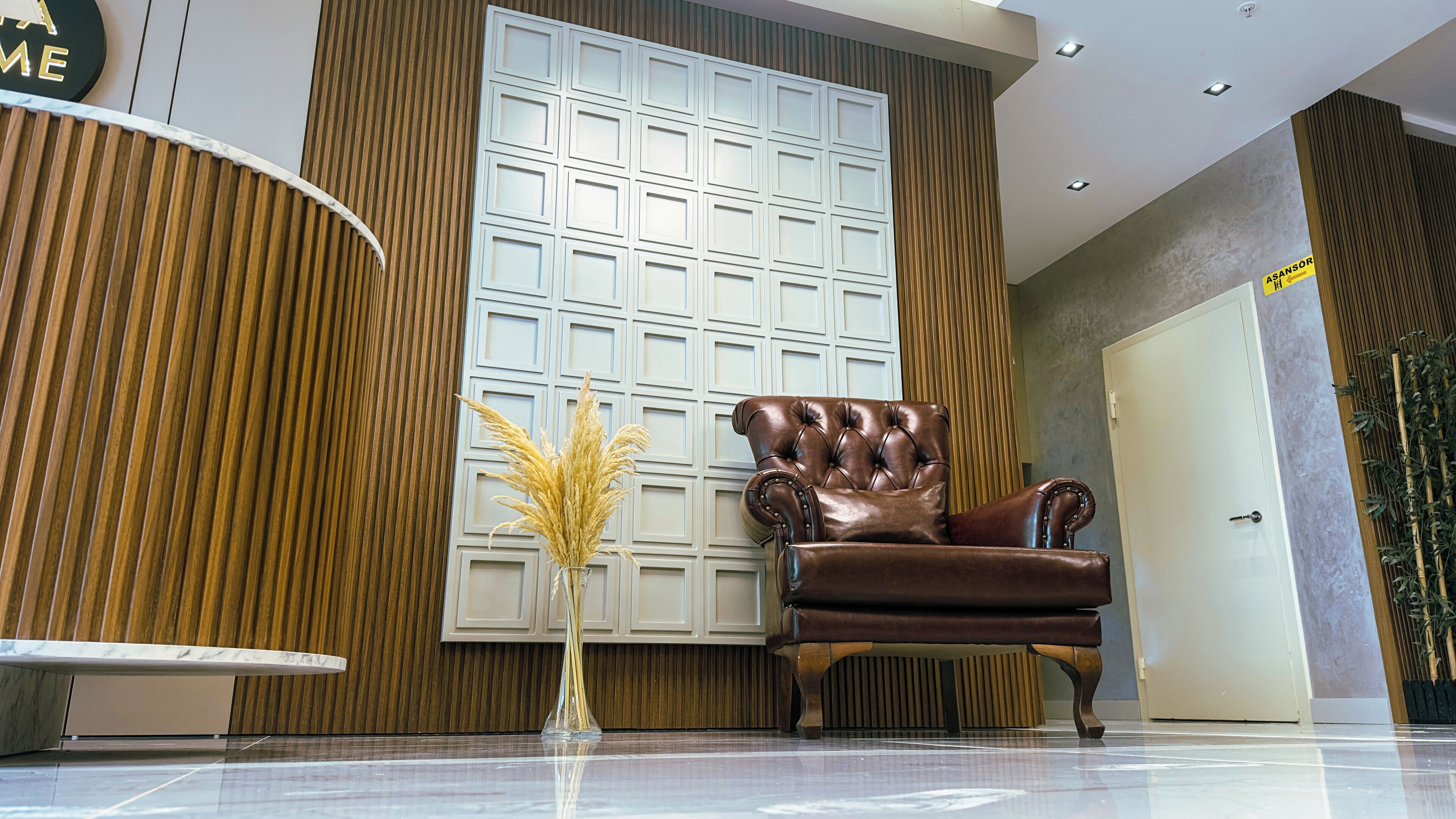 A modern lobby with a leather armchair, a large white panel wall, and a tall plant.