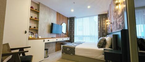 A hotel room with a bed, a desk with a chair, a TV, and a wardrobe.
