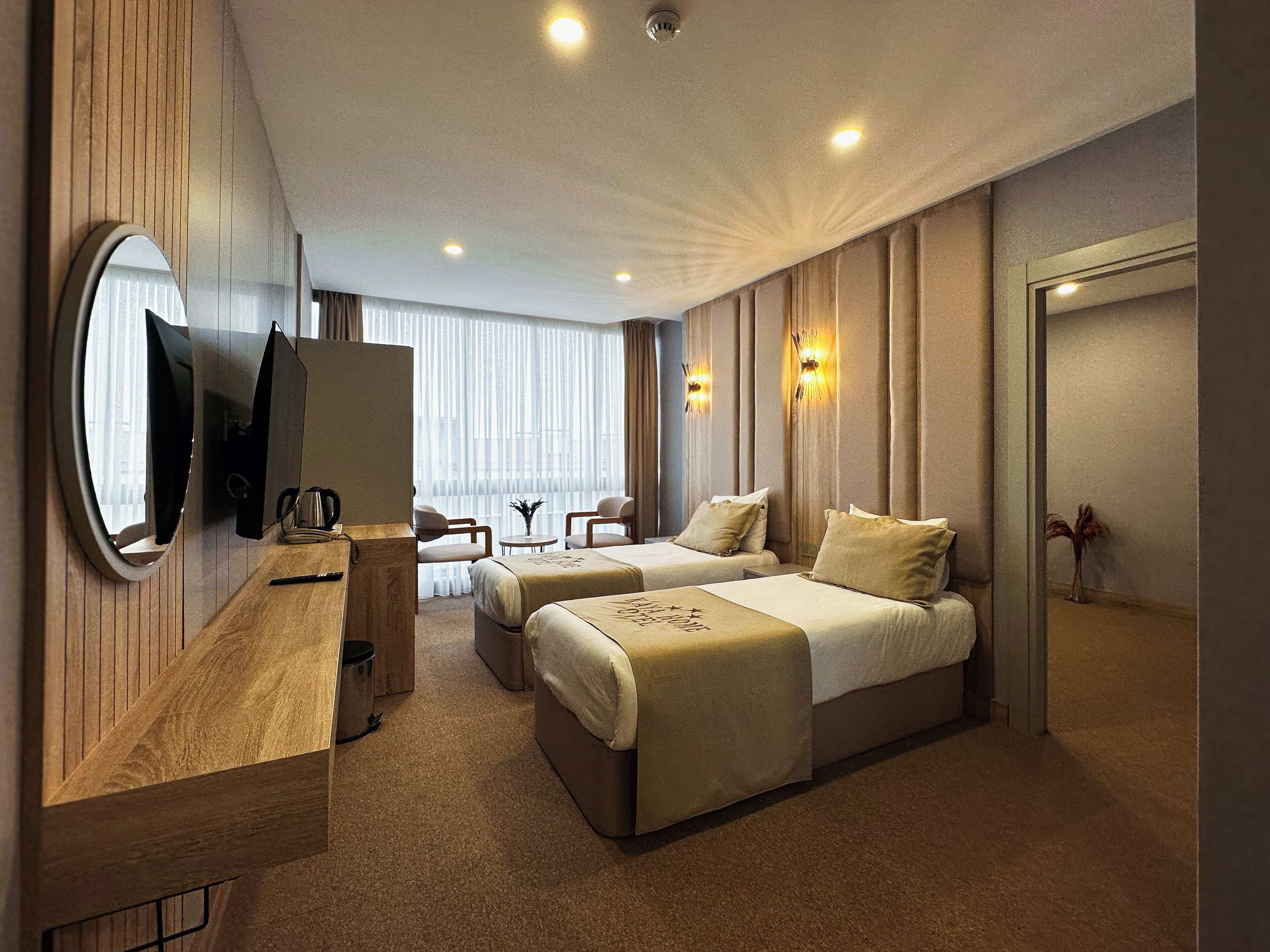 A hotel room with two beds, a wooden desk, a television, and a window with curtains.
