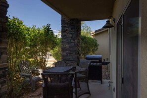 An outdoor patio with a stone pillar, wicker furniture, and a grill.