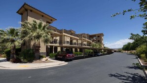 A multi-story hotel with a covered parking area and a palm tree in the foreground.