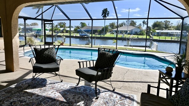 A pool area with two chairs and a rug, overlooking a body of water and a residential area. - Spacious Waterfront Home 3BR 2BA  Heated Pool  Boat Dock & Fishing (Port Charlotte)