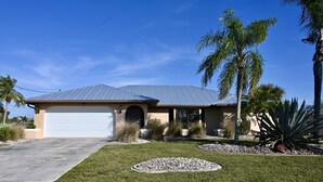 A single-story house with a garage, surrounded by a well-maintained lawn and landscaping. - Spacious Waterfront Home 3BR 2BA  Heated Pool  Boat Dock & Fishing (Port Charlotte)