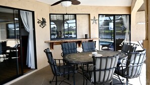 A dining area with a round table and chairs, a ceiling fan, and large windows with curtains. - Spacious Waterfront Home 3BR 2BA  Heated Pool  Boat Dock & Fishing (Port Charlotte)