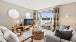 Ein modernes Wohnzimmer mit einer Couch, einem Couchtisch, einem Fernseher und einem Balkon mit Blick.