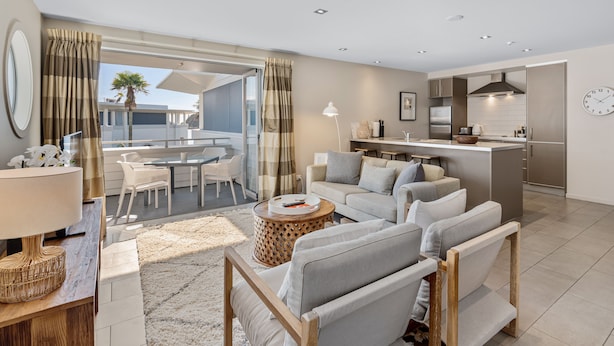 Ein modernes Wohnzimmer mit Sofa, Couchtisch und Essbereich. Im Hintergrund ist eine Küche zu sehen.