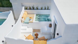 A modern outdoor living area with a hot tub, seating, and a wooden fence. - Electra Suites & Spa (Santorini)