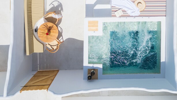 A modern, minimalist room with a large window, a wooden table with chairs, and a view of the ocean. - Electra Suites & Spa (Santorini)