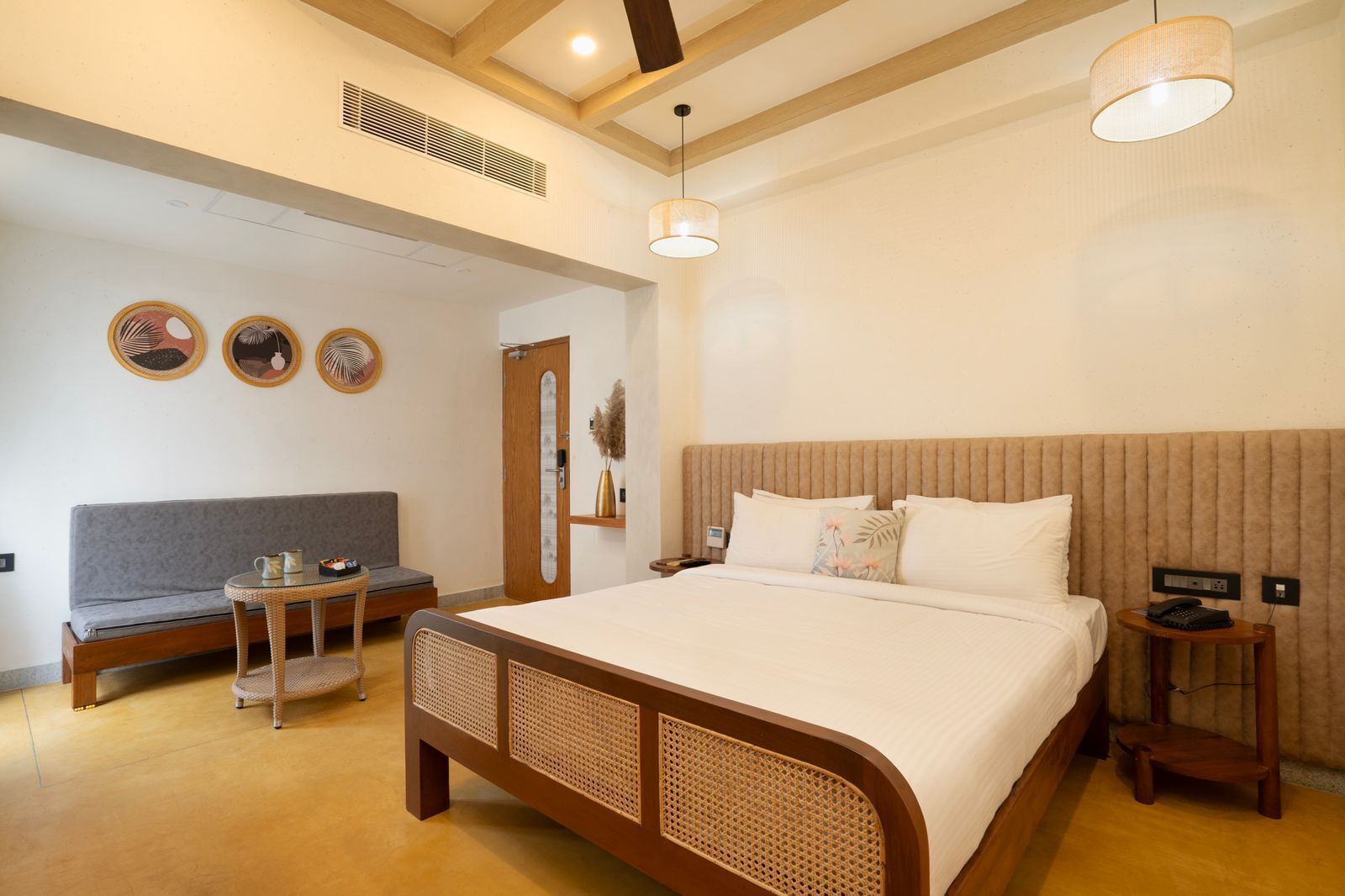 A hotel room with a large bed, a sofa, a small table, and a bedside table with a lamp.
