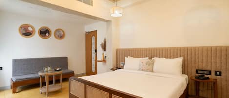 A hotel room with a large bed, a sofa, a small table, and a bedside table with a lamp.