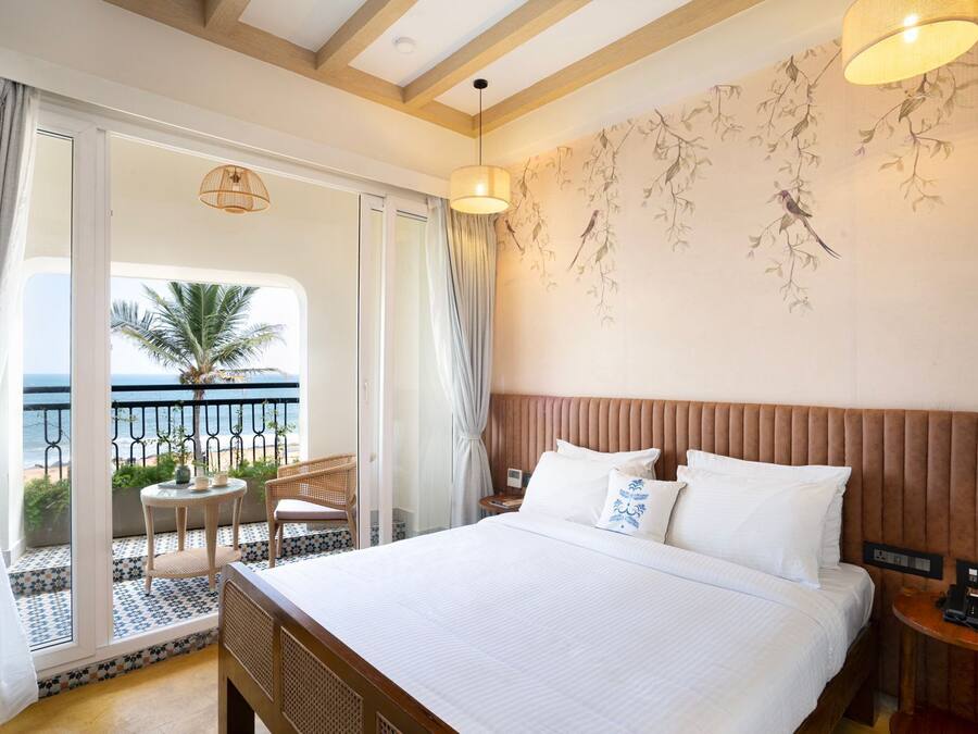 Une chambre d’hôtel avec un grand lit, un balcon donnant sur la mer et une petite table avec des chaises.