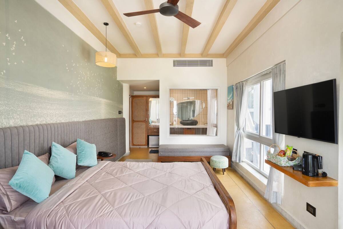 A bedroom with a large bed, a ceiling fan, a TV, and a window with curtains.