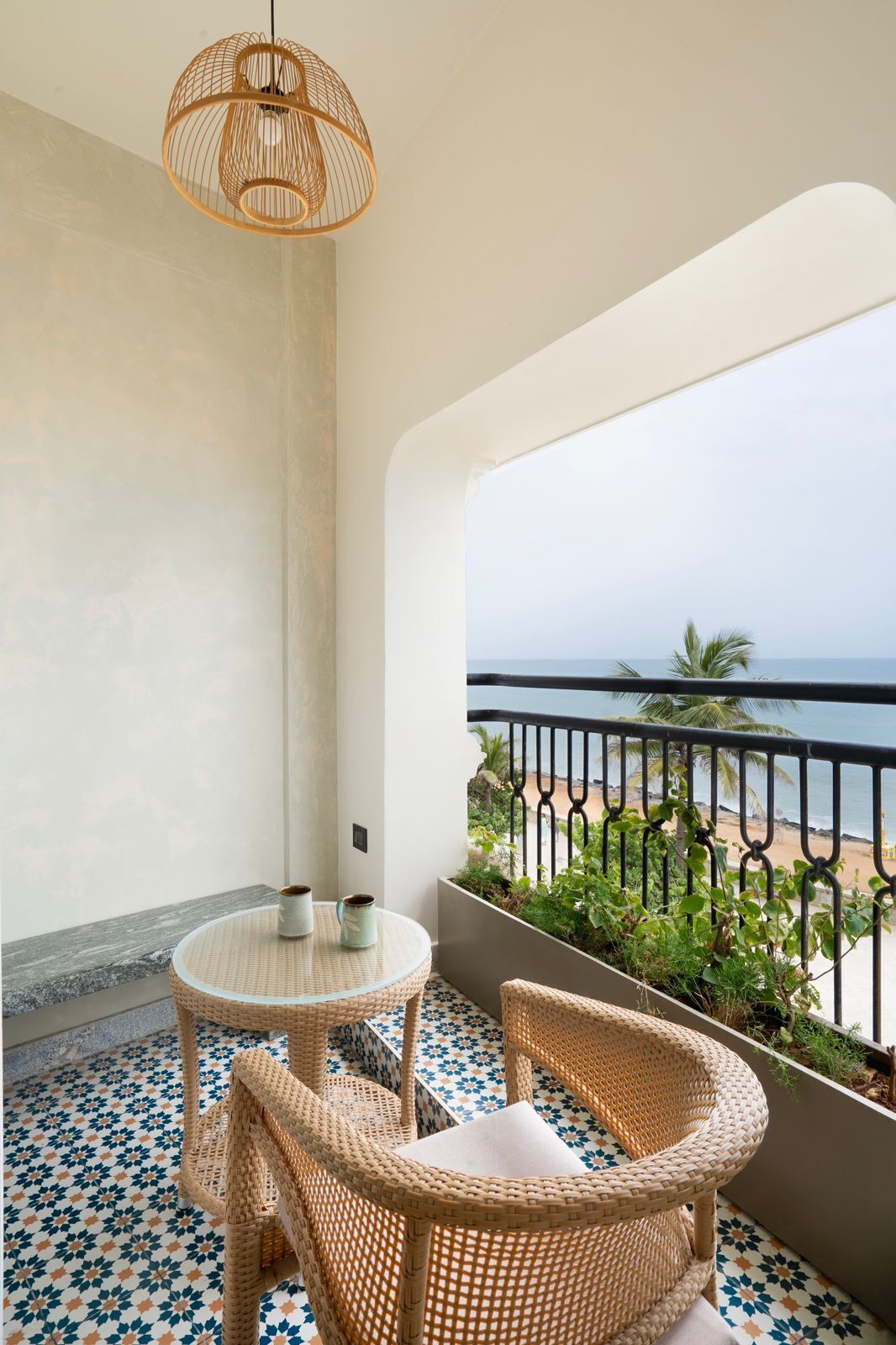 A balcony with wicker furniture, a woven light fixture, and a view of the beach.