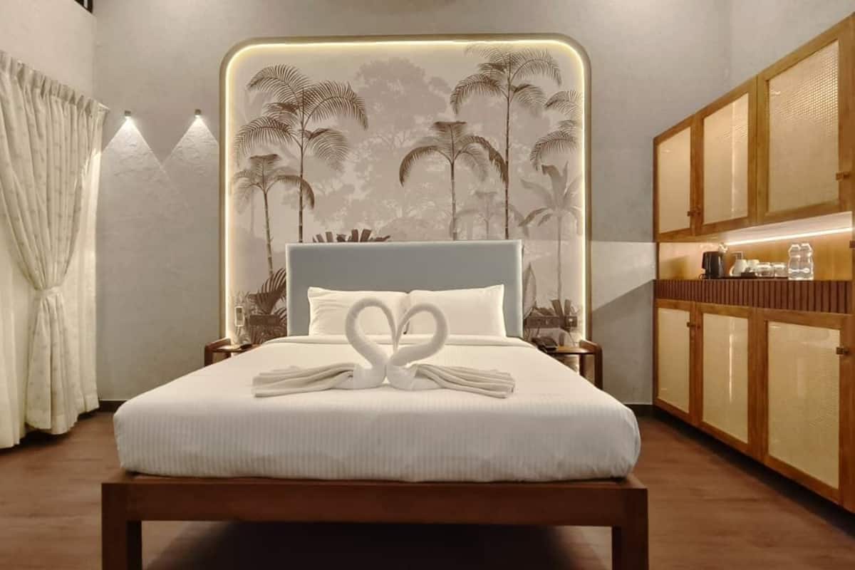 A neatly made bed with a heart-shaped towel, a headboard with a palm tree design, and a wooden wardrobe with a mirror.