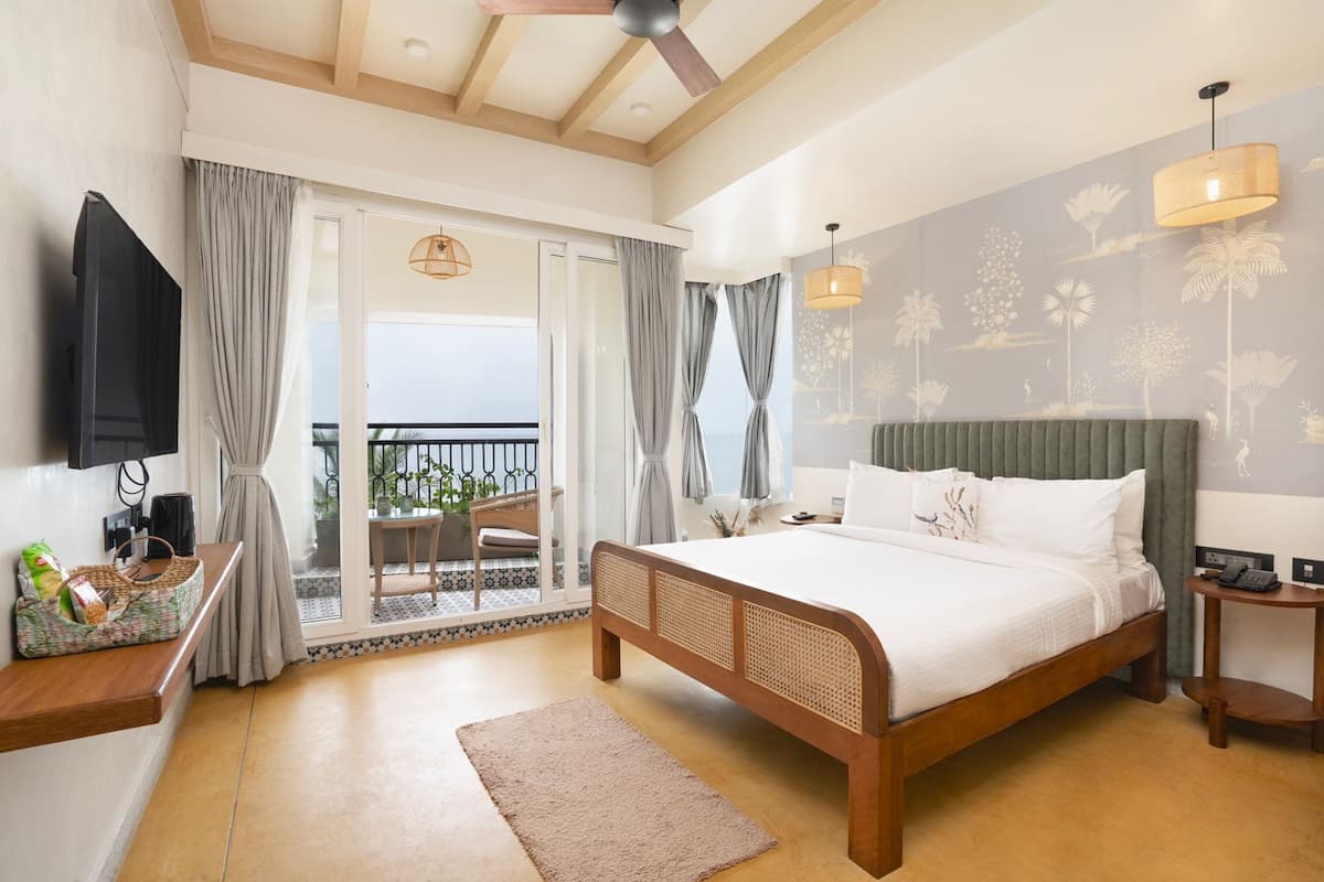 A bedroom with a bed, a TV, a desk, a chair, a balcony, and a view of the sea.