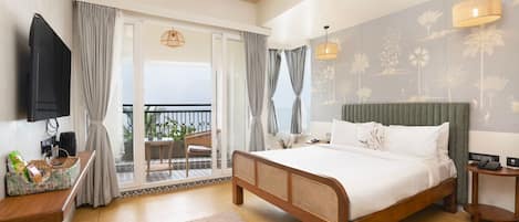 A bedroom with a bed, a TV, a desk, a chair, a balcony, and a view of the sea.