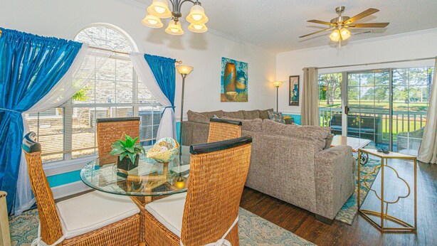 A dining area with a glass table, wicker chairs, a ceiling fan, and a view through large windows. - MP101-Building 22 Magnolia (Myrtle Beach)