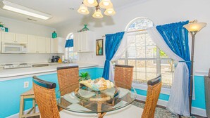 A kitchen with a dining area, white cabinets, a microwave, wicker chairs, and a glass table. - MP101-Building 22 Magnolia (Myrtle Beach)