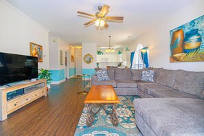 A living room with a television, sofa, coffee table, and ceiling fan.