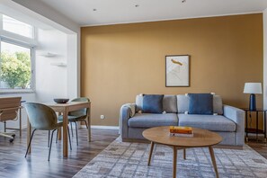 Relax in this stylish living room with a sofa, coffee table, and dining area, offering a view of lush greenery.