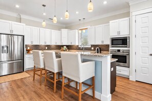 A modern kitchen with white cabinets, stainless steel appliances, and a bar area with bar stools.