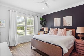 A bedroom with a bed, a nightstand, a lamp, a ceiling fan, and a window with blinds.