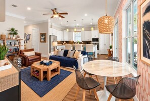 A modern living room with a sofa, coffee table, and chairs, a dining area with a round table, and a kitchen in the background.