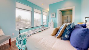 A bedroom with a bed, a nightstand, a window with blinds, a ceiling fan, and a door leading to a bathroom.