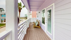 A covered porch with wooden chairs, a white railing, and a view of the beach.