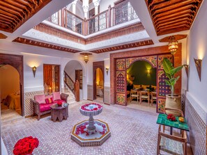 A luxurious interior with a central fountain, a dining area, and a staircase leading to an upper level. - Riad Kilimini & SPA (Marrakech)