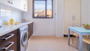 A compact kitchen with a washing machine, a window, and a dining area with a table and chairs. - Holidays2Malaga Heroe de Sostoa with pool view (Málaga)