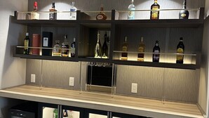 Zona de bar con estantes llenos de botellas de licores, un minibar y un refrigerador.