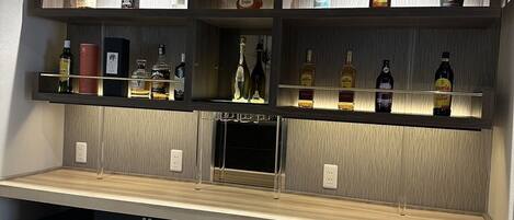 A bar area with shelves of liquor bottles, a minibar, and a refrigerator.